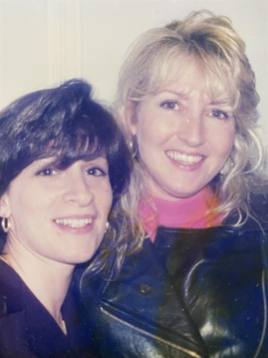 Two friends share a joyful smile, capturing a warm memory at a casual event in the 1990s.
