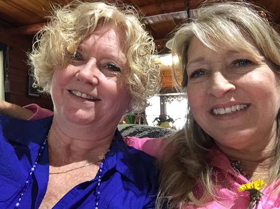 Two friends smile closely together at a friendly gathering in a rustic setting.