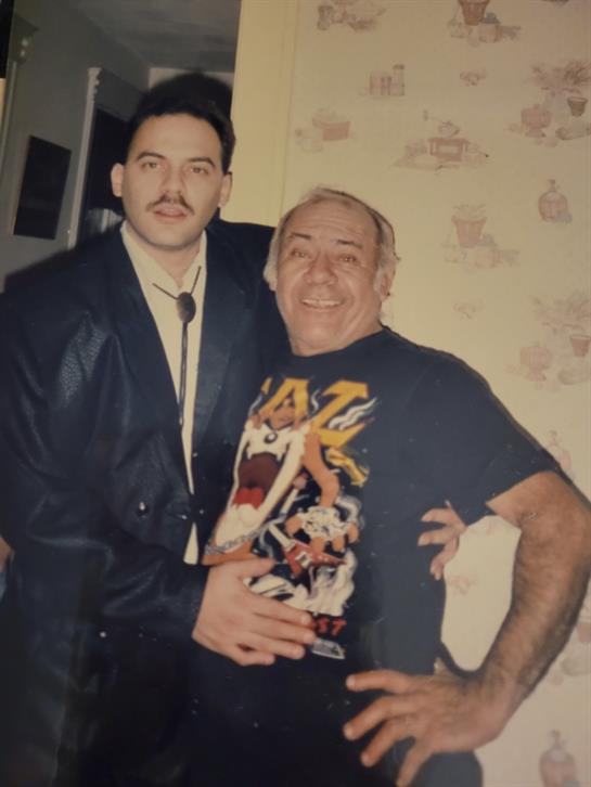 Two men smile and pose closely together in a cozy, patterned room, sharing a joyful moment.