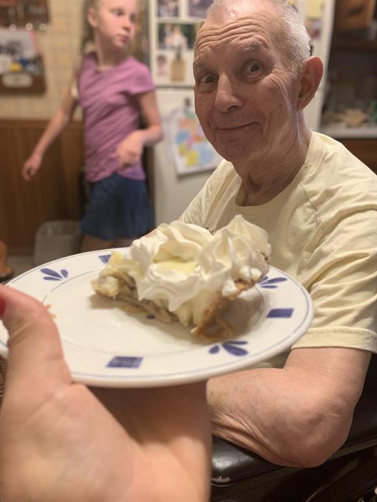 Family members celebrate together as an elderly man smiles while holding a dessert at home.