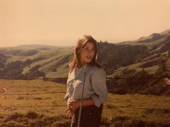 A woman enjoyes the view of lush hills while standing in a golden light at sunset.