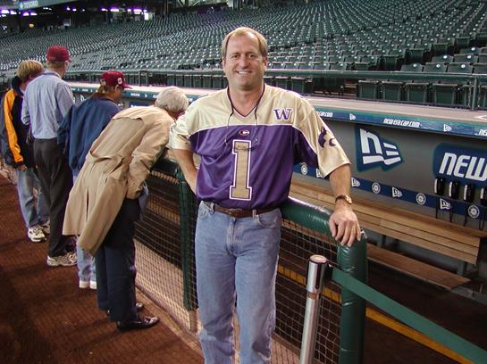 A passionate sports fan stands at the dugout, surrounded by empty seats and fellow fans.