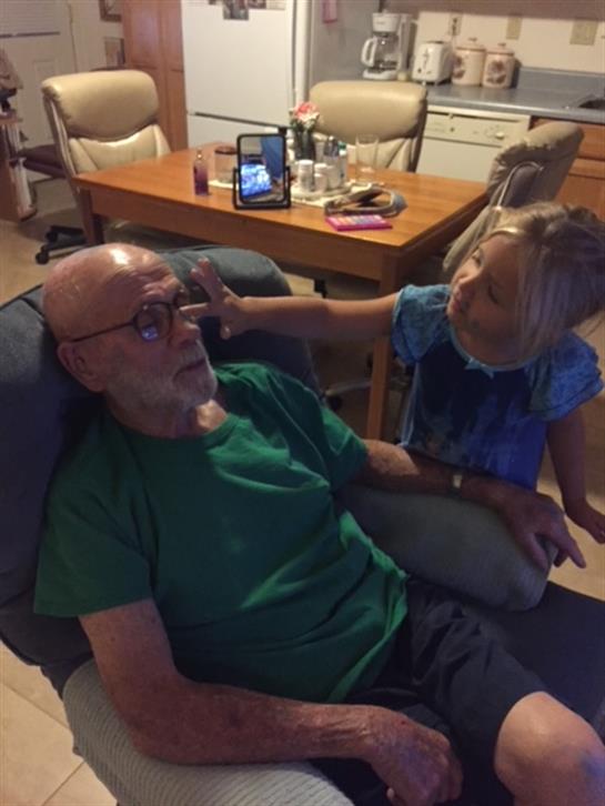 A young girl playfully interacts with her grandfather while he relaxes on a chair in the evening.