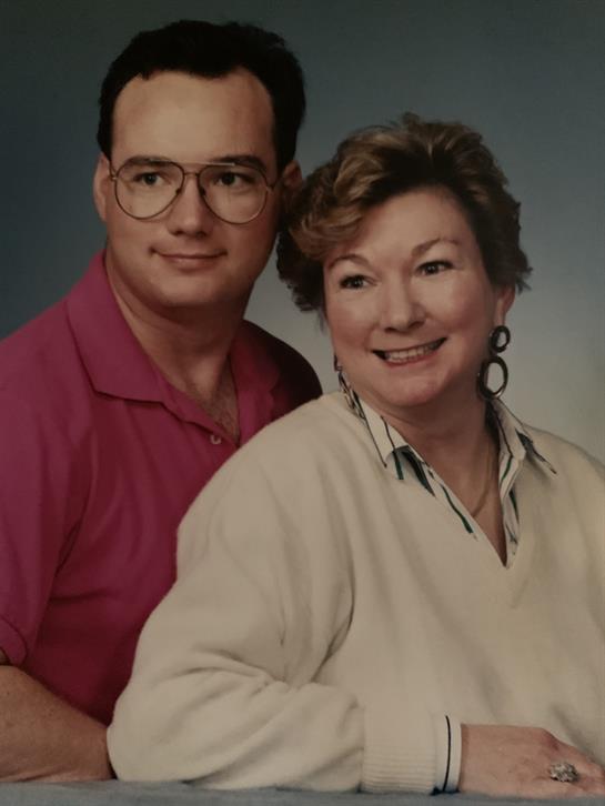 A cheerful couple poses together, smiling warmly at the camera, in a studio environment.