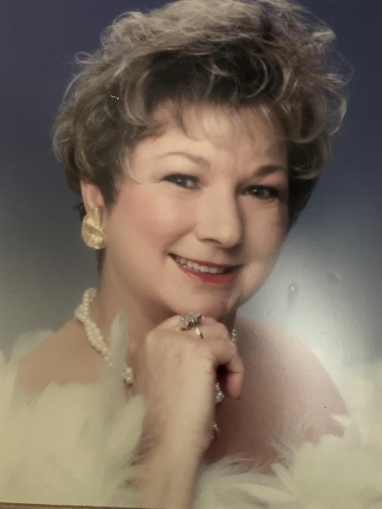 A smiling woman with curly hair and pearl jewelry shows elegance and confidence in a gentle light.