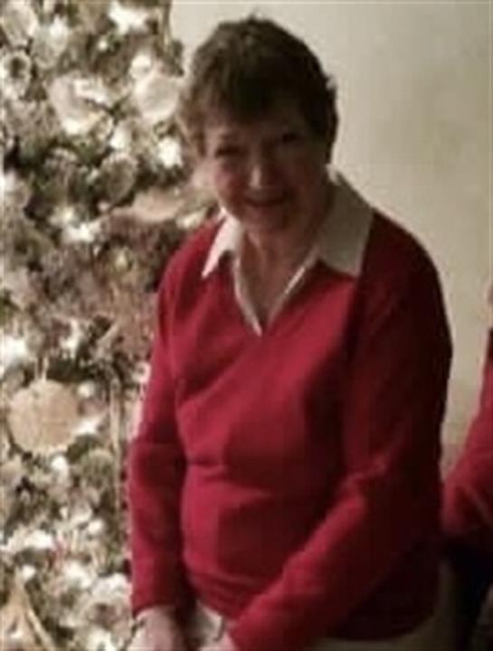 A joyful woman in a red sweater enjoys a festive moment by a decorated Christmas tree.