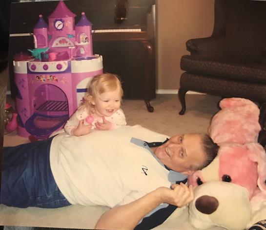 A happy toddler is playing on the floor with her grandfather near a large stuffed bear and toys.