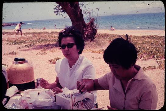Friends relax and share food during a picnic on the sandy beach near the ocean.