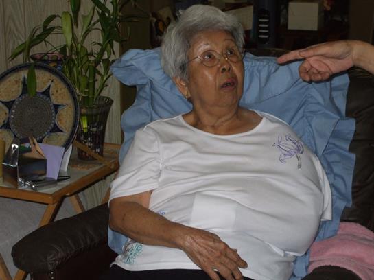An elderly woman reacts with surprise while seated in a comfortable chair during a family gathering.
