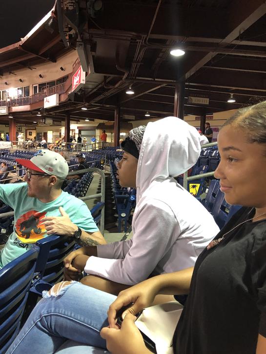Friends seated in the stands, chatting and watching an exciting baseball game unfold.