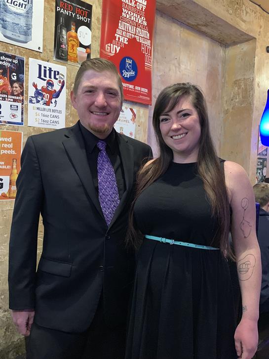 Man in a suit and woman in a dress smile while surrounded by vibrant bar decor.