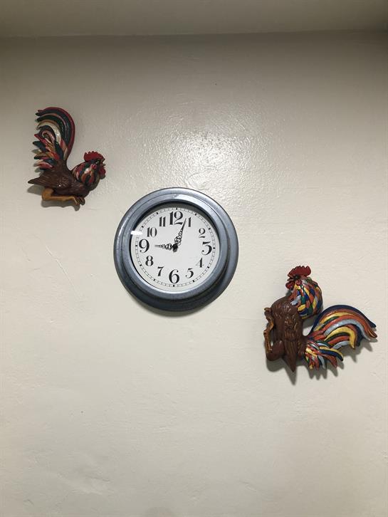 Rooster decorations flank a round wall clock in a warm kitchen environment, creating a rustic feel.