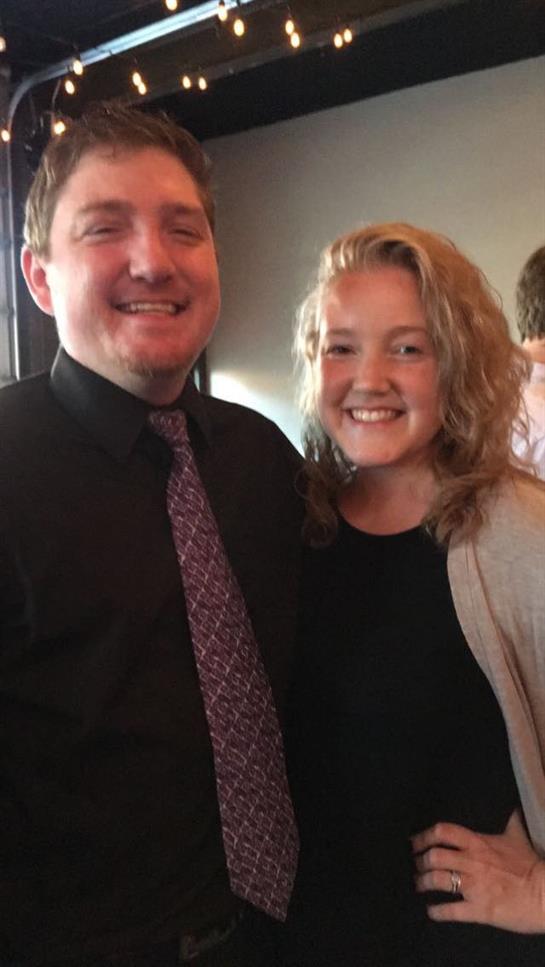 Two smiling individuals pose closely together, enjoying a joyful moment at a gathering.