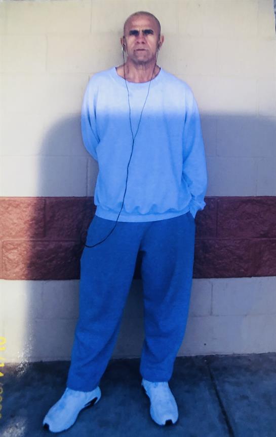 Person in blue clothing listens to music while standing by a wall.