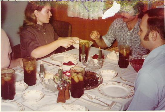 Two people share a meal at a dining table filled with food and beverages in a cozy setting.