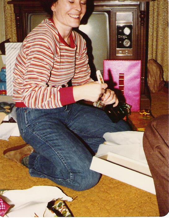 A child kneels on the carpet, focused on wrapping gifts while surrounded by festive decorations.