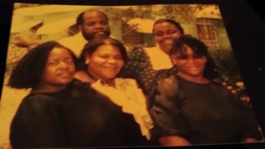 Six cheerful individuals are gathered outdoors, enjoying a casual family reunion with smiles.