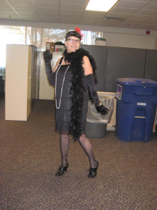 A woman in a glamorous 1920s outfit poses stylishly at her workplace for a themed event.