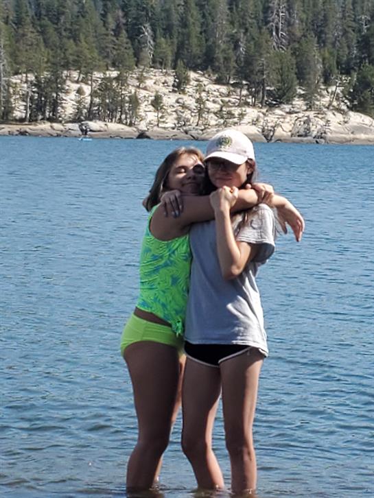 Two friends embrace while standing in a lake, enjoying their time together in the sun.