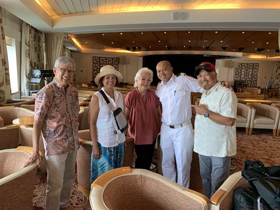 A cheerful group of five friends stands together in a lounge, smiling and chatting happily.