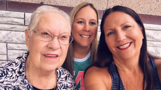 Three women smile joyfully while standing outdoors during a family gathering in summer.