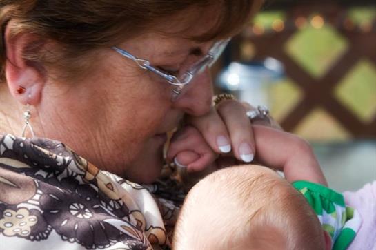 Grandmother gently holds baby's hand, expressing warmth and affection in a serene garden.