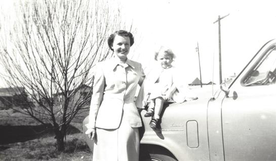 A woman and a smiling child enjoy a sunny day while posing next to a classic truck.