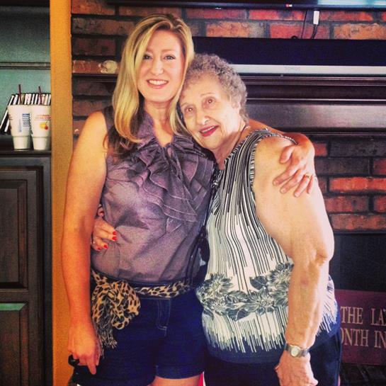 Two women smile and pose closely together, joyfully celebrating their bond in a warm space.