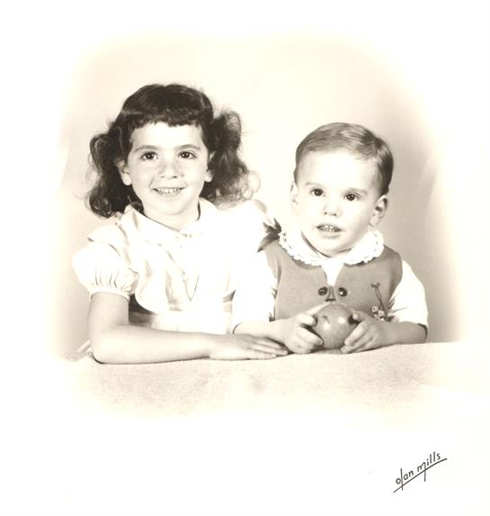Two young children smile together, sitting side by side with a toy object on the table.