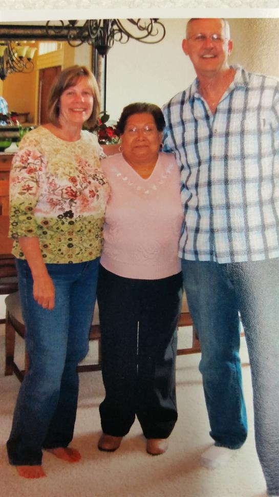 Three family members stand together, smiling warmly in a comfortable home environment.