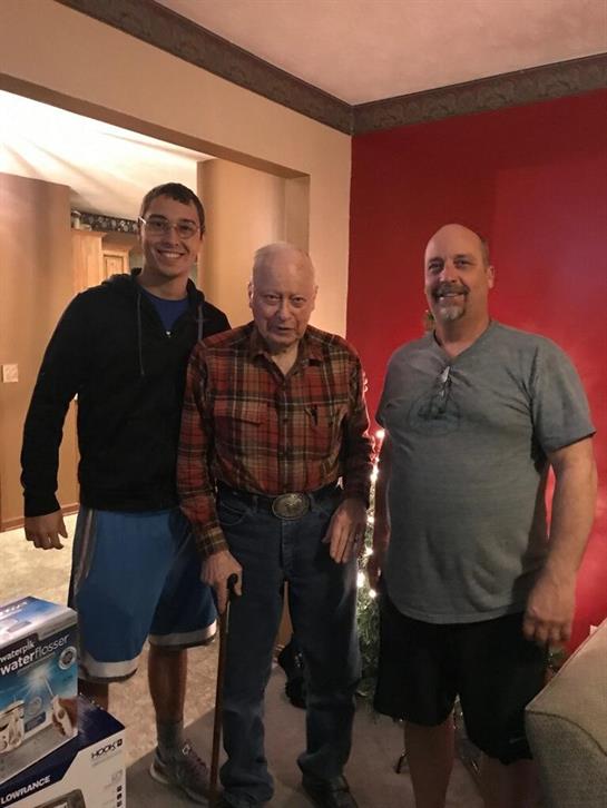 Three men stand together in a cozy indoor space, enjoying a moment of family connection.