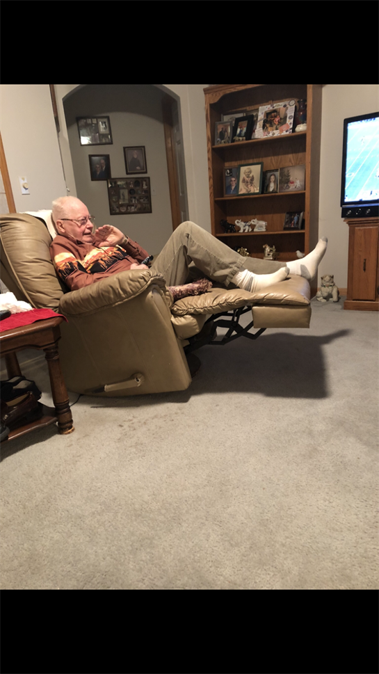 A senior man enjoys his leisure time in a recliner, focused on his favorite television show.