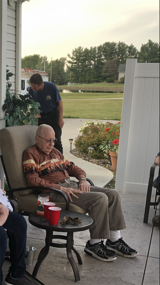 Elderly people relax on a porch, enjoying refreshments and conversation on a warm afternoon.