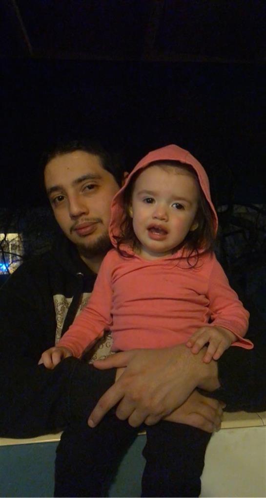A man embraces a toddler wearing a pink hoodie, both sharing a gentle moment at night.