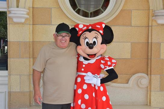 A man stands happily with a friendly animated character in a cheerful outfit, both smiling.