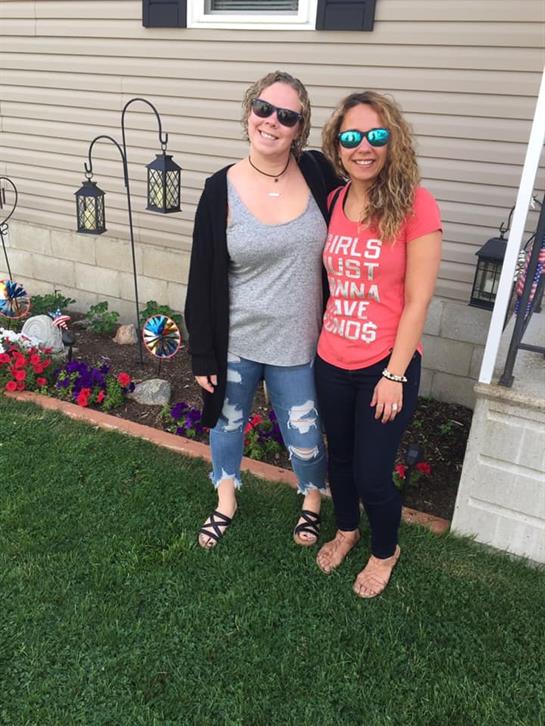 Two women stand smiling in a garden surrounded by colorful flowers and decorative lanterns.