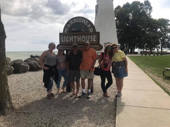 A group of friends poses together at the Waterford lighthouse as clouds gather overhead.