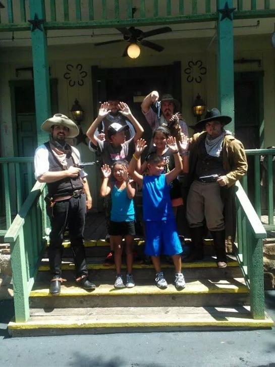 Children joyfully pose with cowboy actors at a western-themed event in a historic venue.
