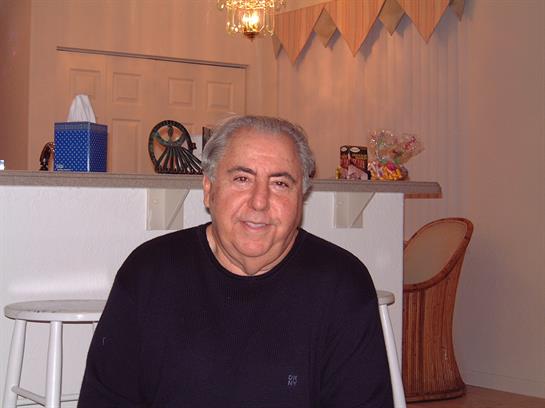 A senior man sits comfortably in a softly lit room, enjoying a moment of relaxation after dinner.