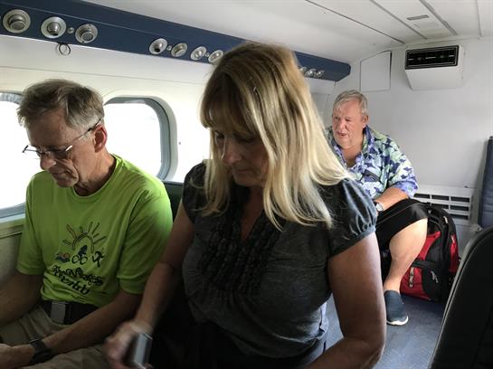 Passengers focus on their belongings while seated inside a small aircraft, ready for departure.
