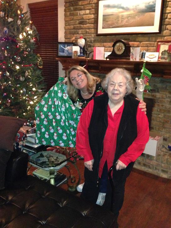 Two women enjoy Christmas in a warmly decorated living room with a tree and gifts.
