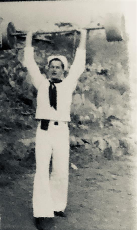 A sailor lifts his arms in a strength exercise against a natural background.