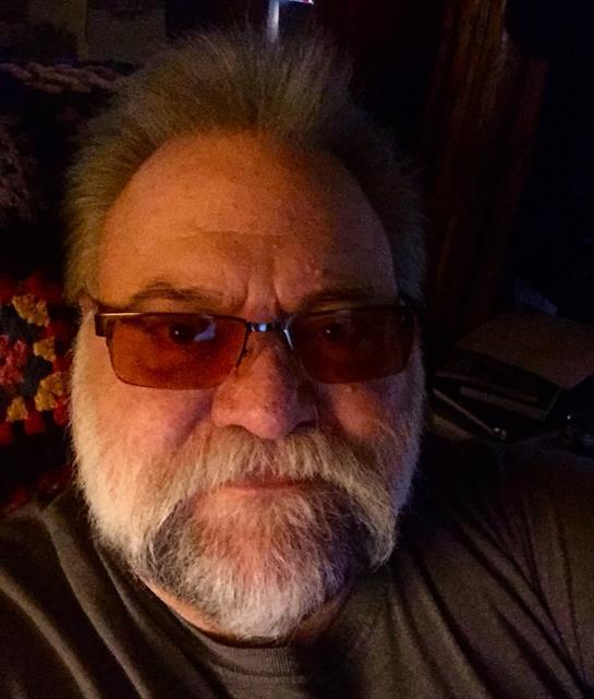 A gray-haired man in sunglasses sits cozily, looking directly at the camera.