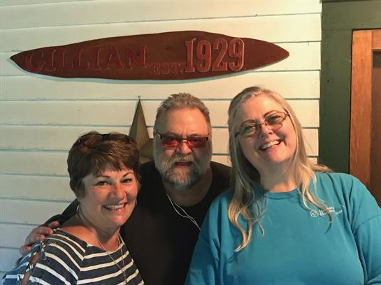 Three friends smile and celebrate together in a nostalgic setting featuring a wooden sign.