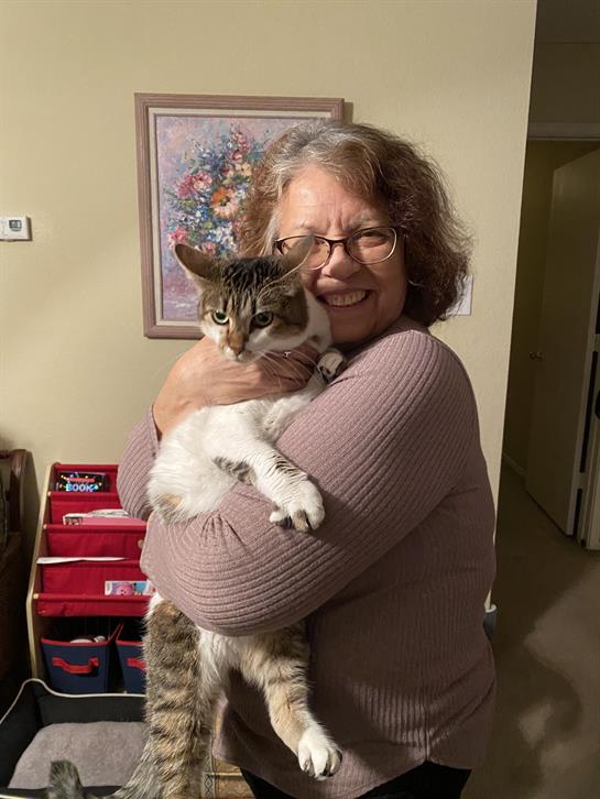 A joyful woman embraces a cat in a warm indoor environment, showcasing a moment of affection.