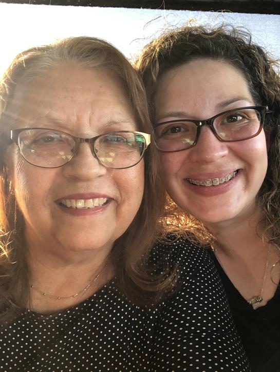 Two women share smiles in a warm, sunny setting, capturing a joyful moment together.