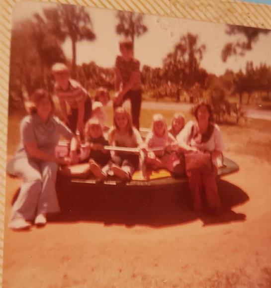 Children and adults gather on a colorful merry-go-round, laughing under the sun at a park.