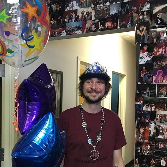 A joyful person holds festive balloons in a hall filled with photo memories at a celebration.