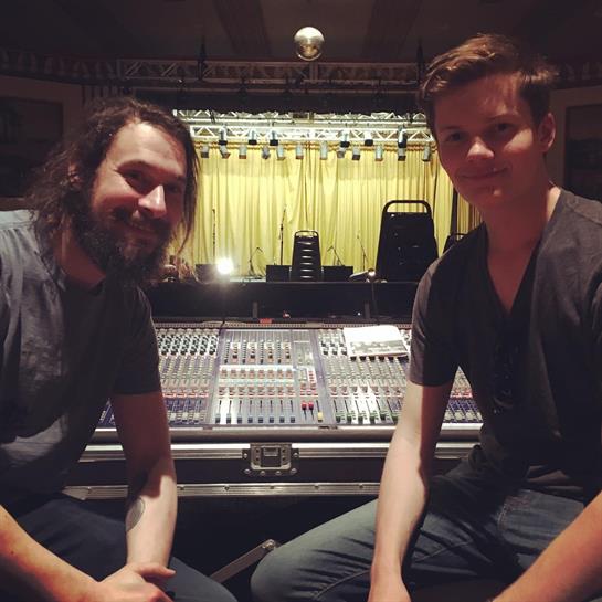 Two musicians smile while seated in front of a sound mixing console before the show.