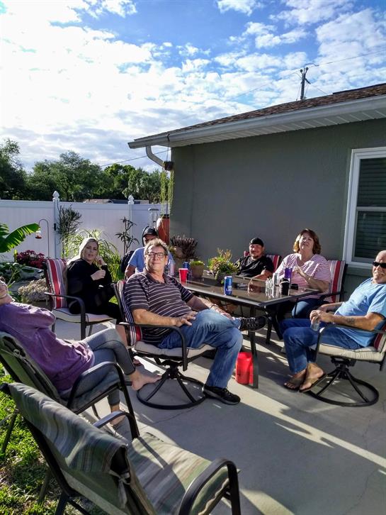 Group of friends relaxes on a patio, engaging in conversation and enjoying drinks in the sun.